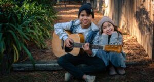 boy holding dreadnought acoustic guitar beside girl during daytime