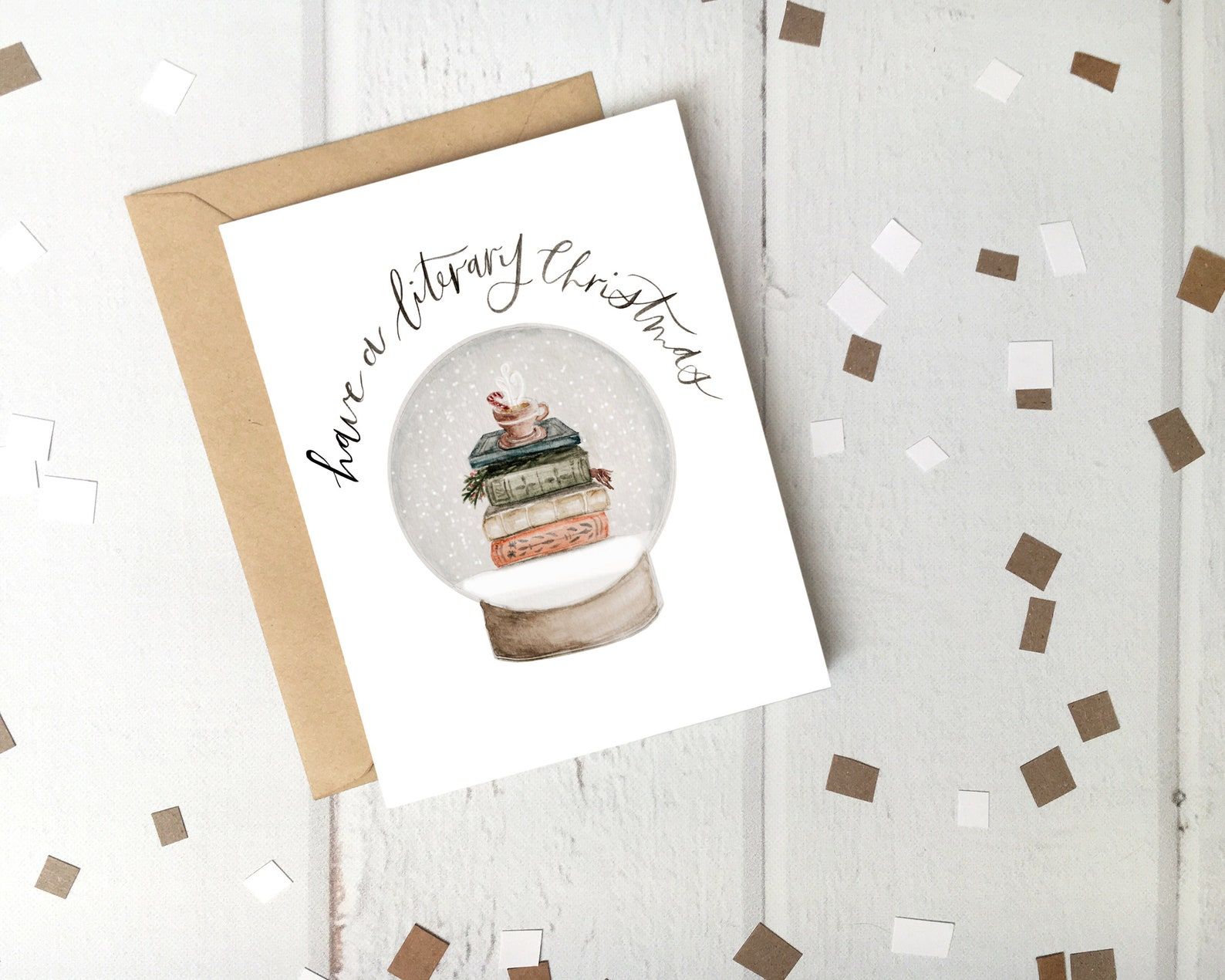A white card reads "Have a literary Christmas" and depicts a snowglobe with a stack of books and a cup of hot cocoa inside.