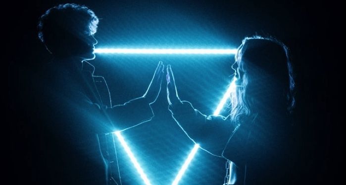 image of teen boy and girl joining hands in front of a blue neon triangle