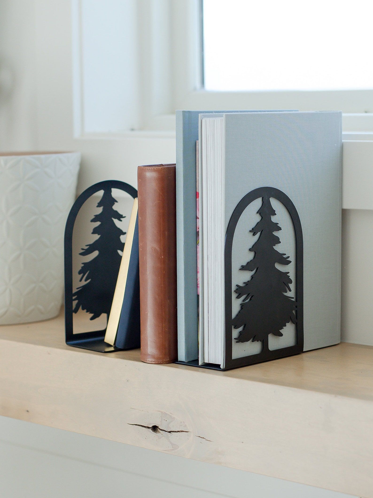 A pair of black steel bookends shaped like spruce trees on a small shelf of books.