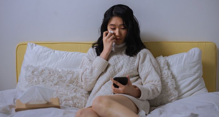 a woman crying in bed while looking at her mobile phone