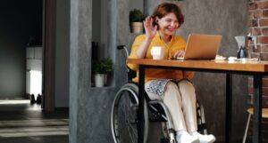 a person in a wheel chair waving in greeting at her laptop screen