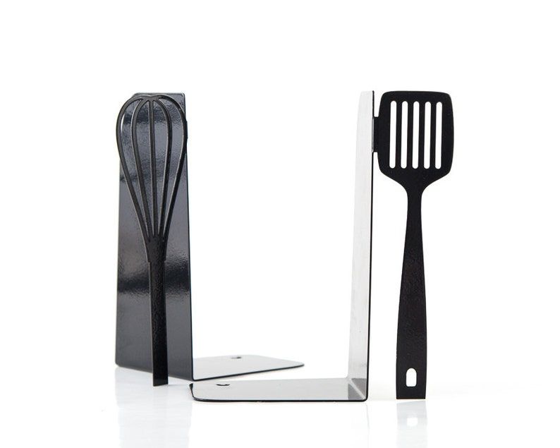 Two metal bookends; one with an upright whisk and the other with an upright spatula.