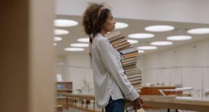 a woman carrying a large stack of books