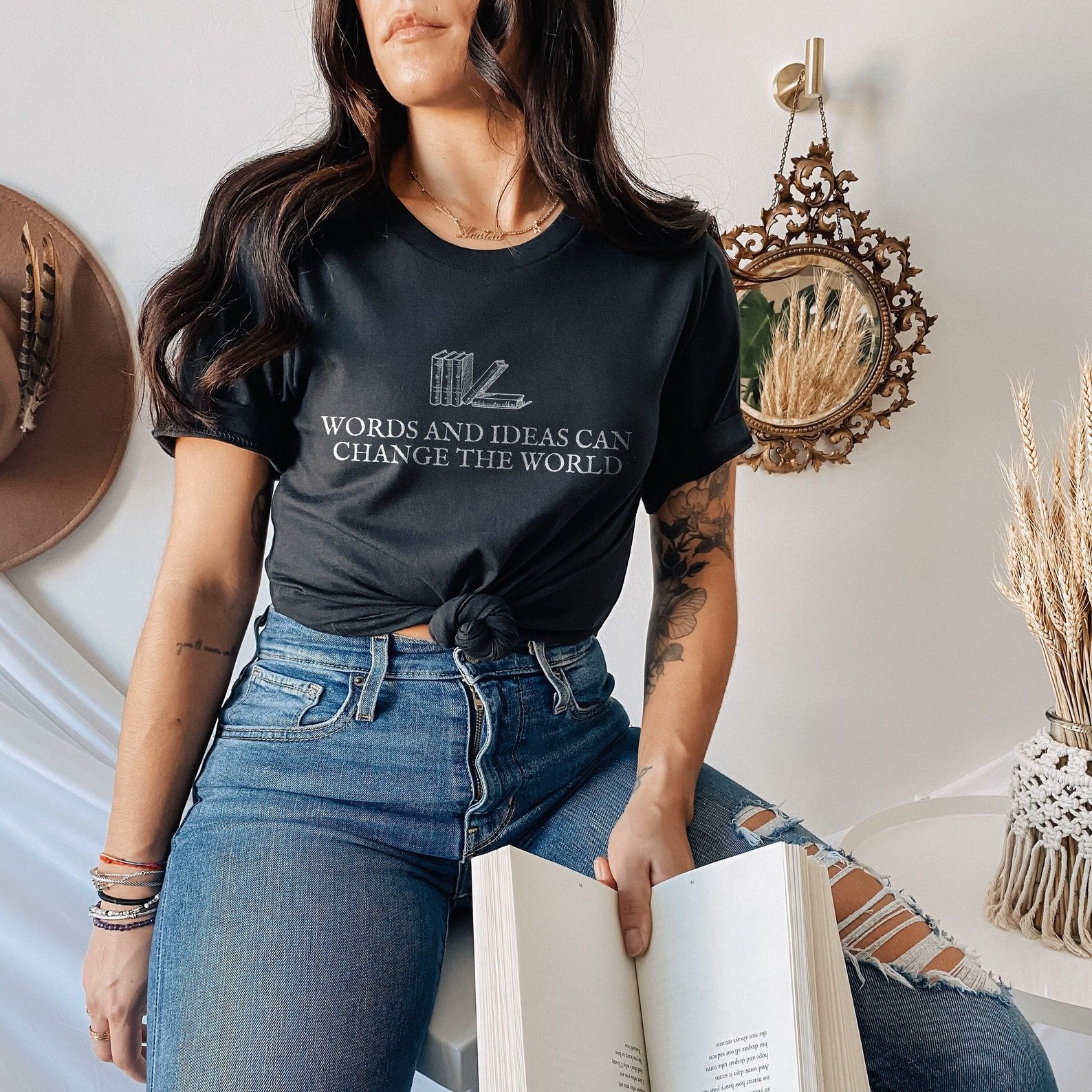 Image of a woman wearing a shirt that reads "words and ideas can change the world." The shirt is black with books on it. 