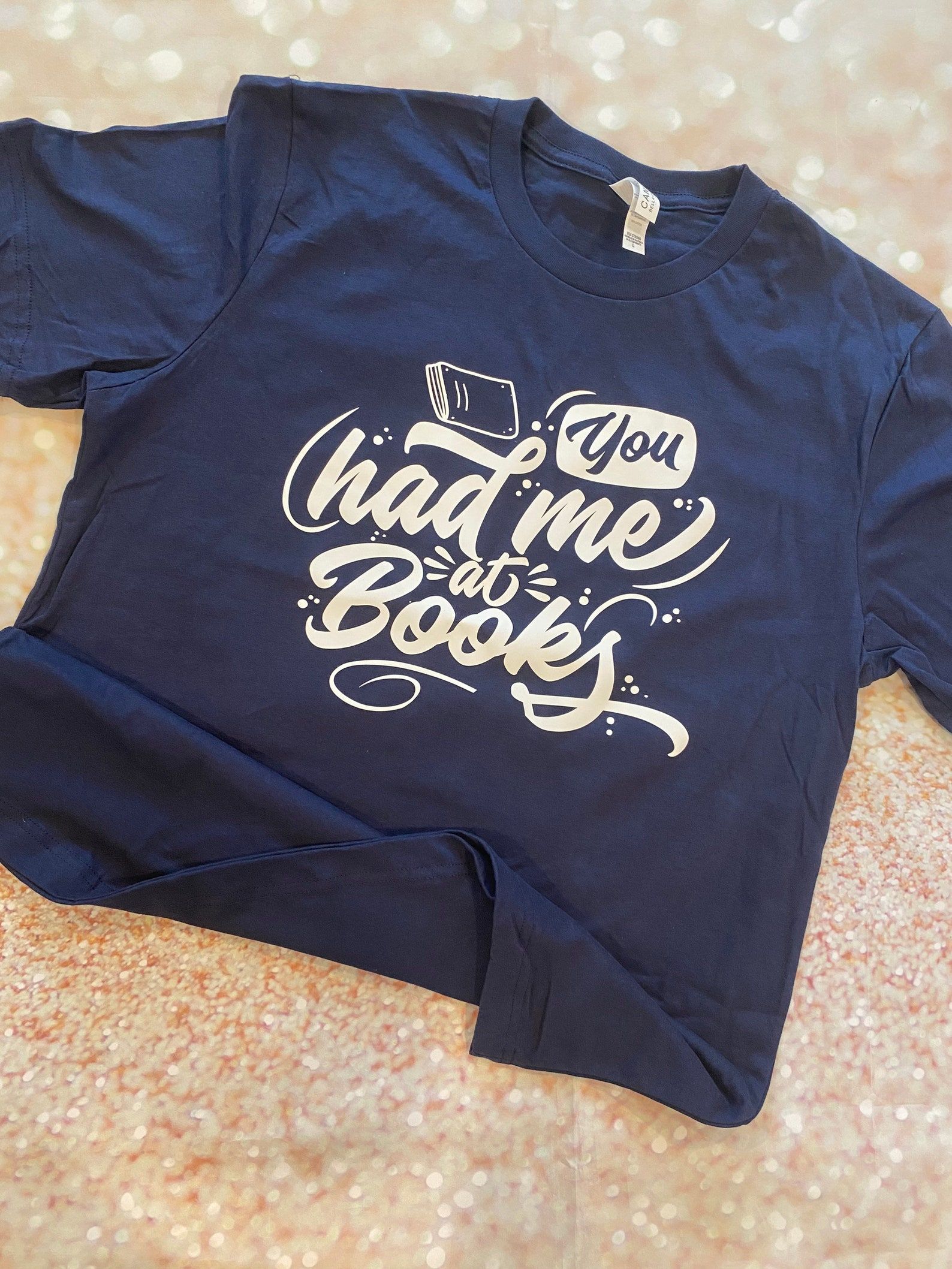 Image of a blue shirt that reads, in script font, "you had me at books."