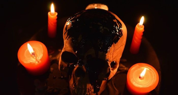 a photo of lit candles glowing orange against a black backdrop, surrounding an orange and black skull