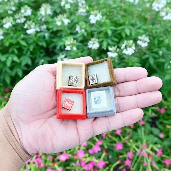 A hand holding four tiny books in tiny boxes