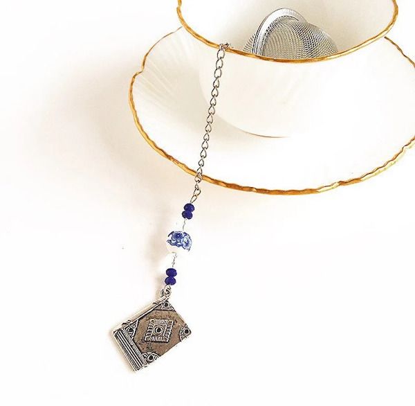 image showing a tea cup with a tea infuser inside and a book-shaped charm on the infuser chain 