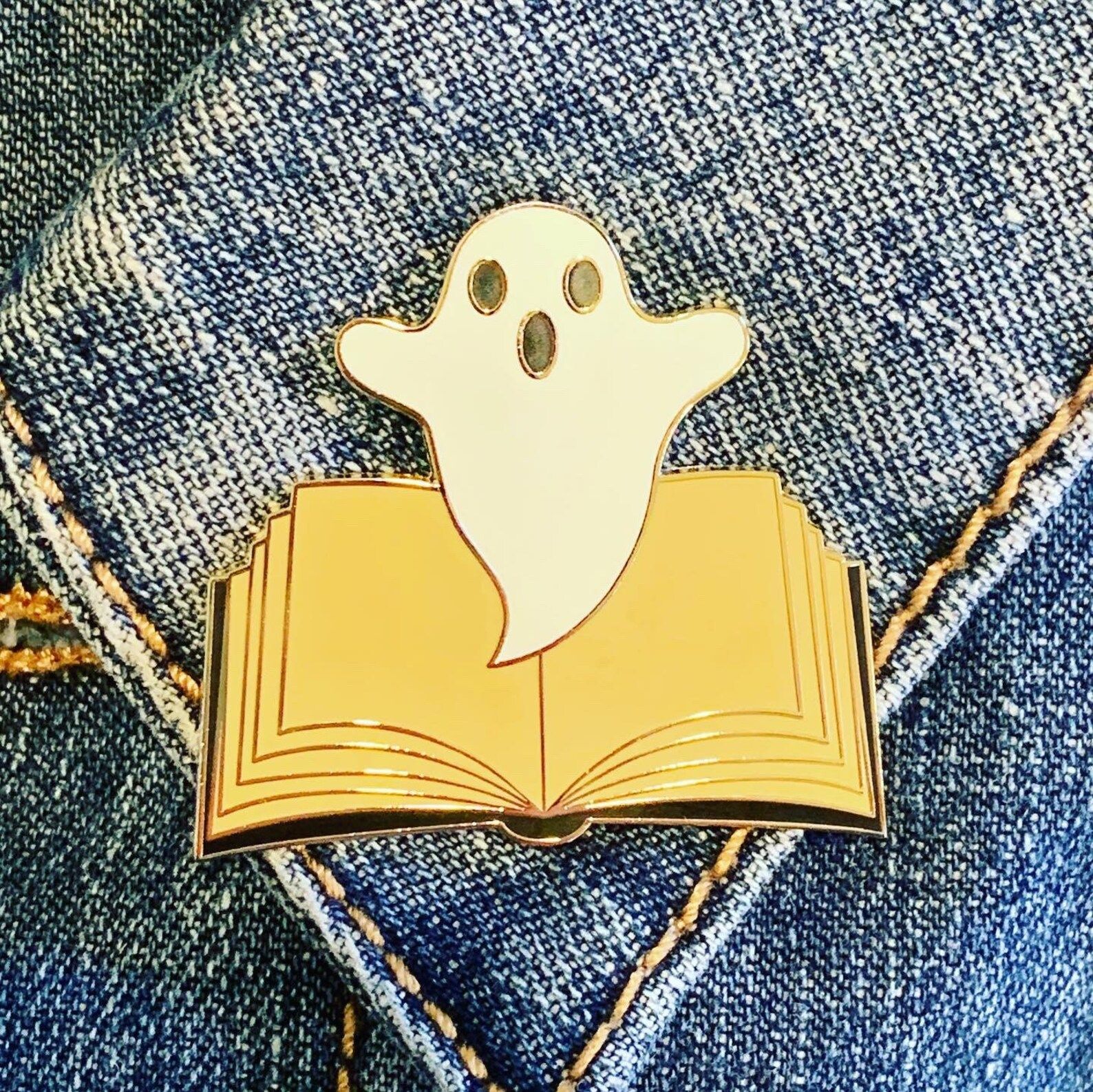 A pin of a small white ghost floating out of an open book.