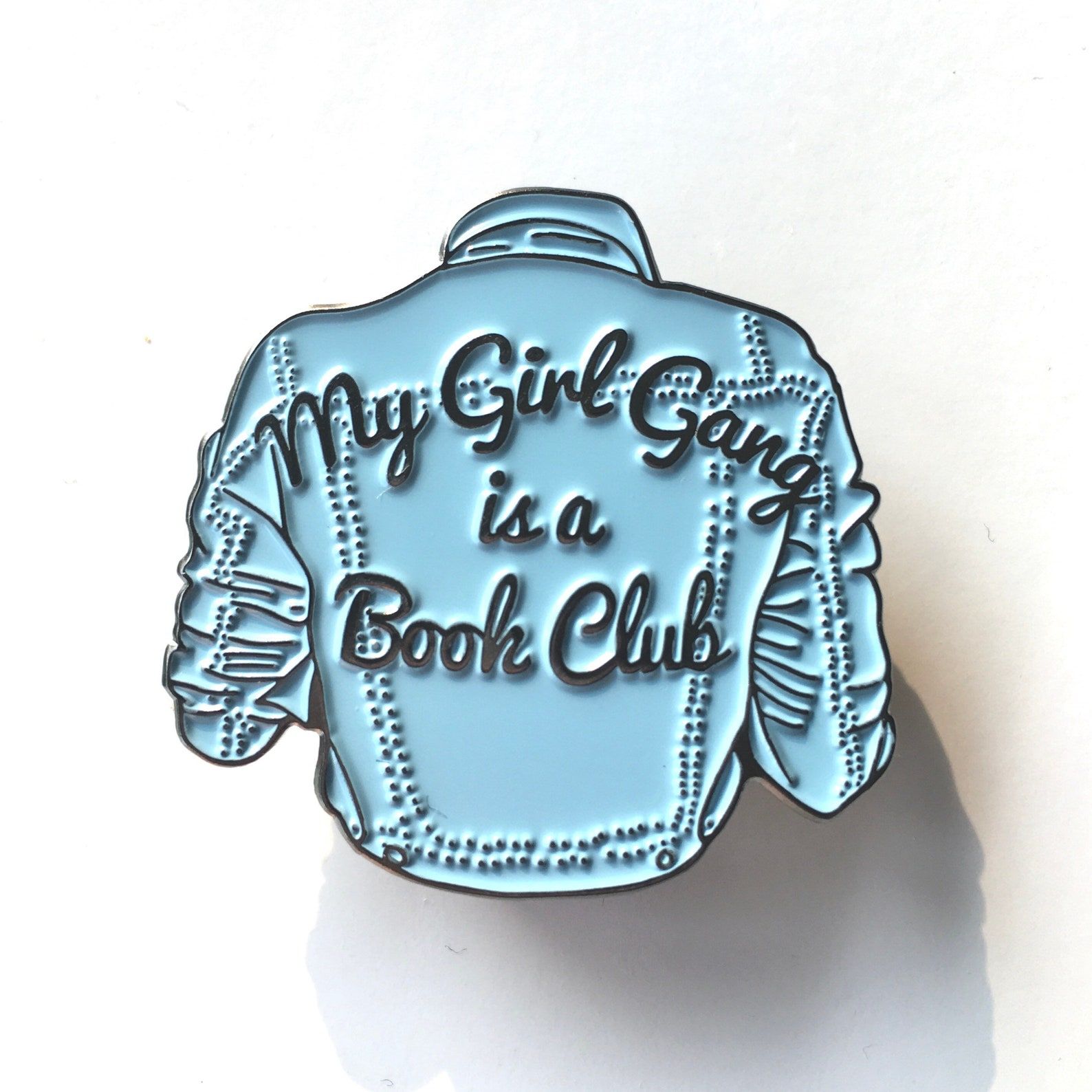 pin shaped like a denim jacket with the words "my girl gang is a book club"