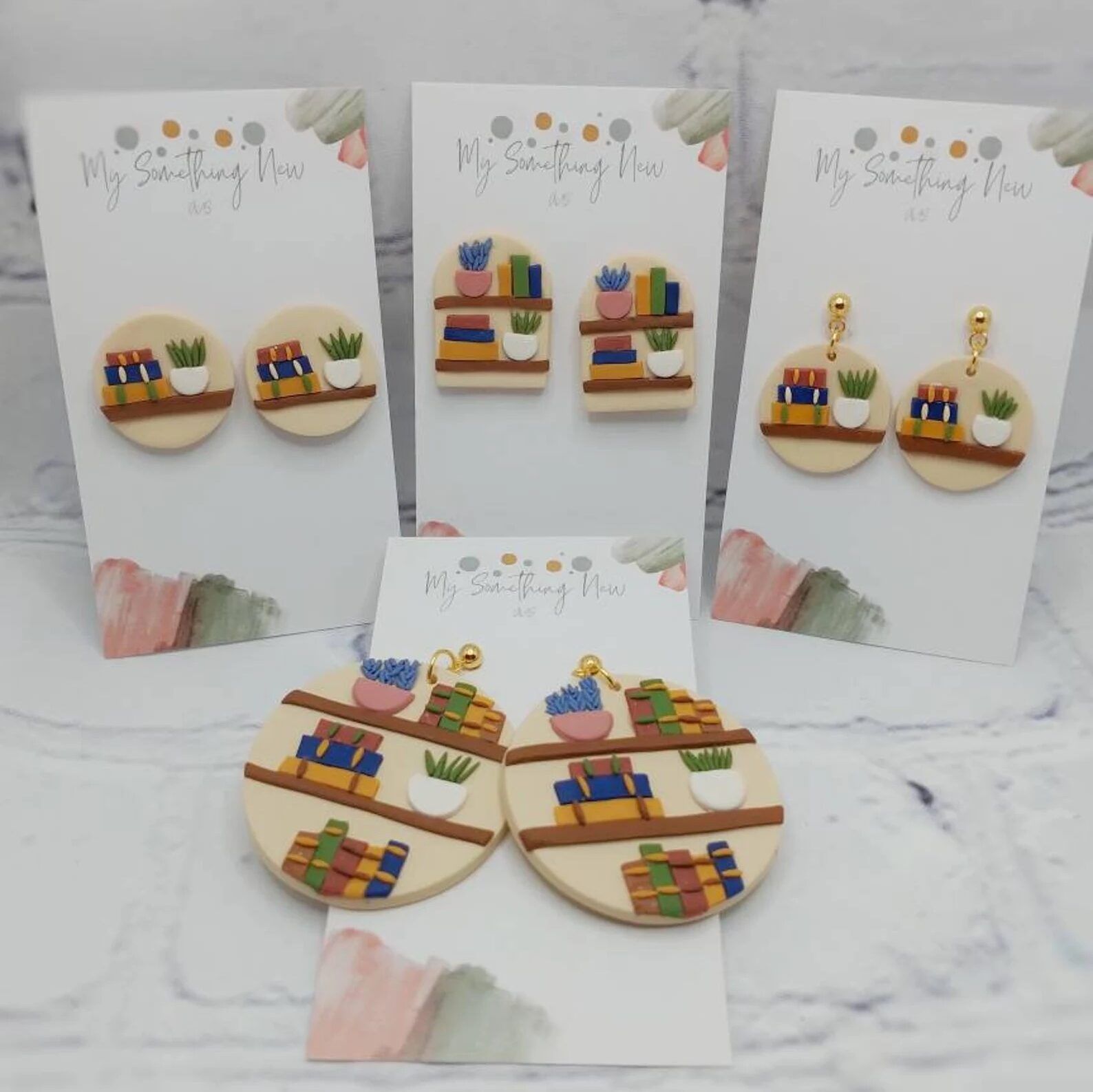 Five pairs of earrings decorated with multicolored books and plants.