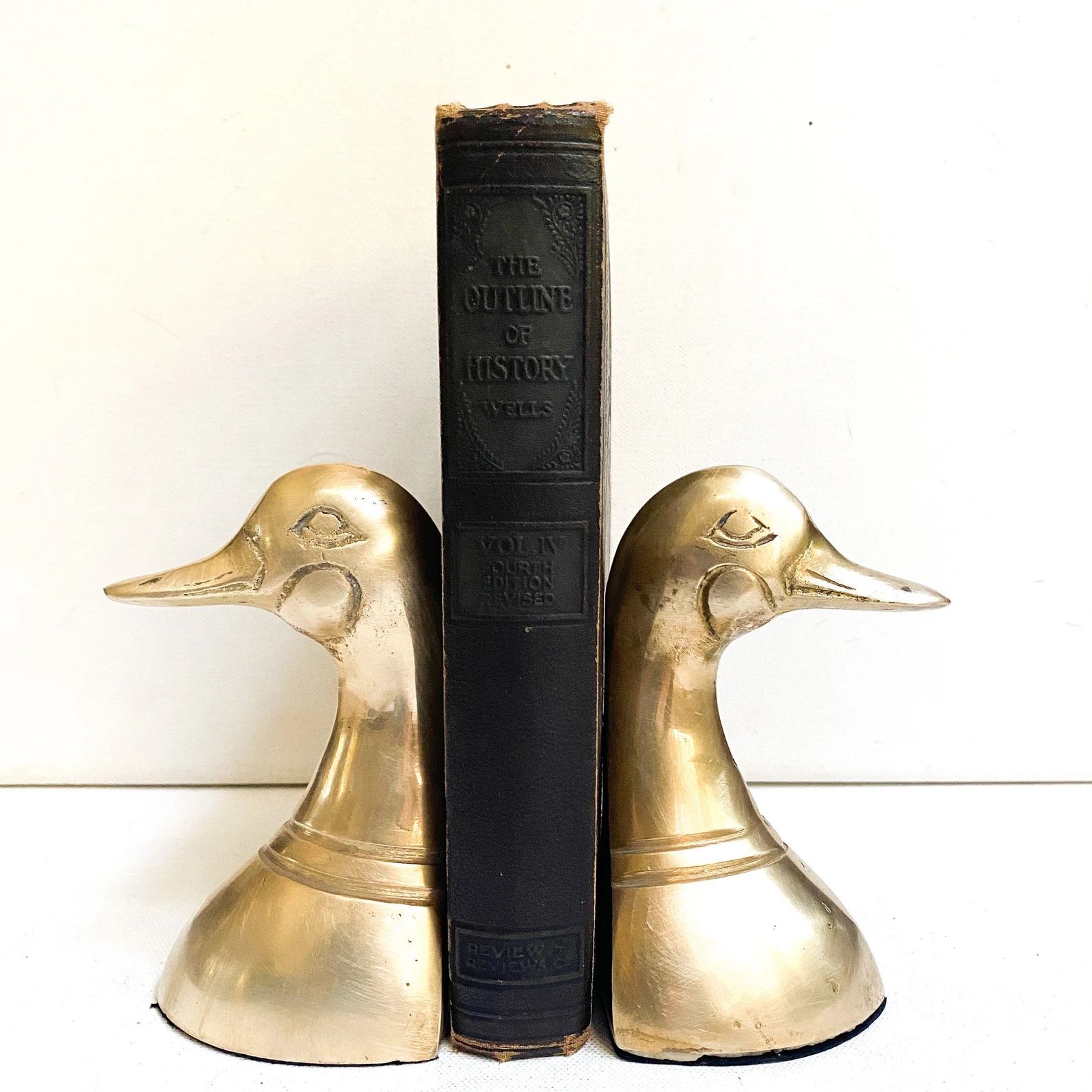 Gift for book lover: Two golden duck book ends on either side of a dark brown vintage book.