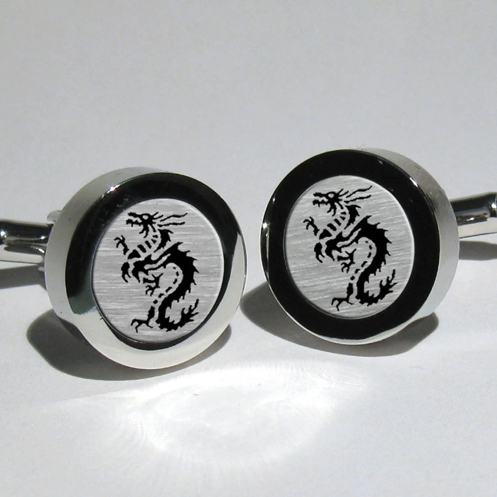 Silver and black cufflinks with dragons on them.