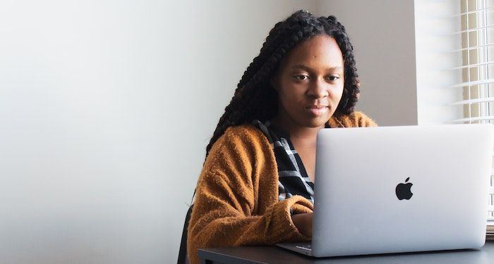 Image of a Black woman in a yellow sweater using a laptop
