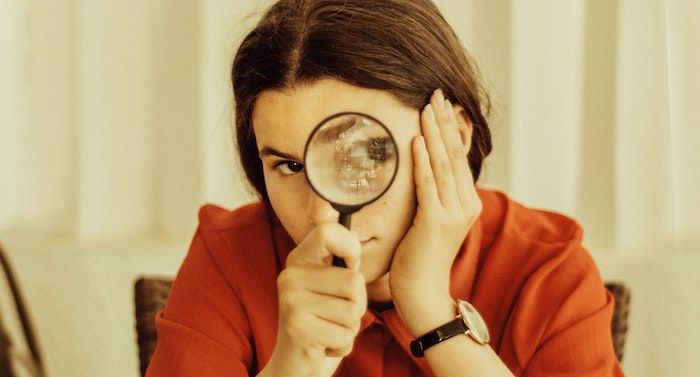 vintage style image of a girl with brown hair and olive skin holding a magnifying glass