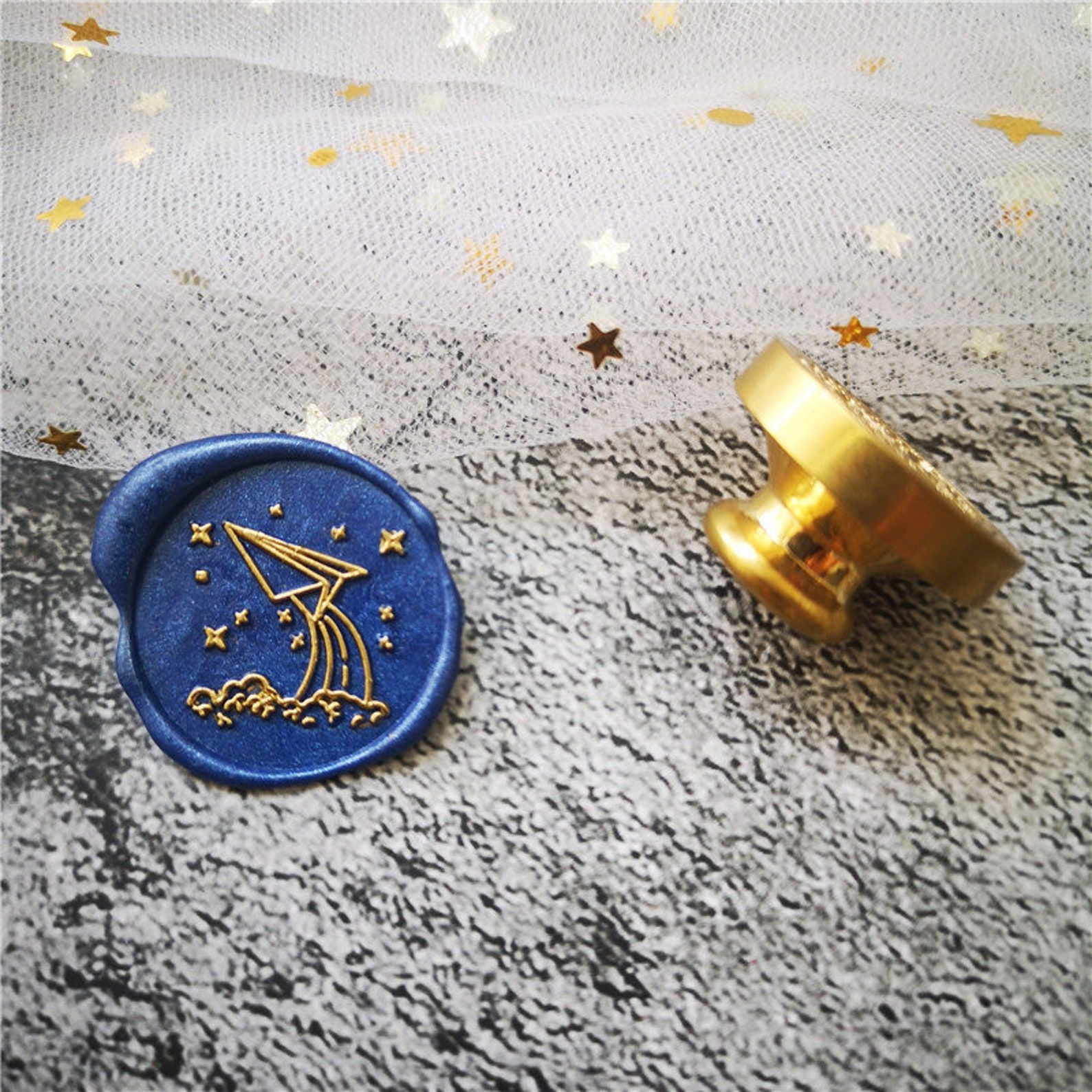 Image of a blue wax seal stamp. The seal is beside it, featuring a paper airplane. 