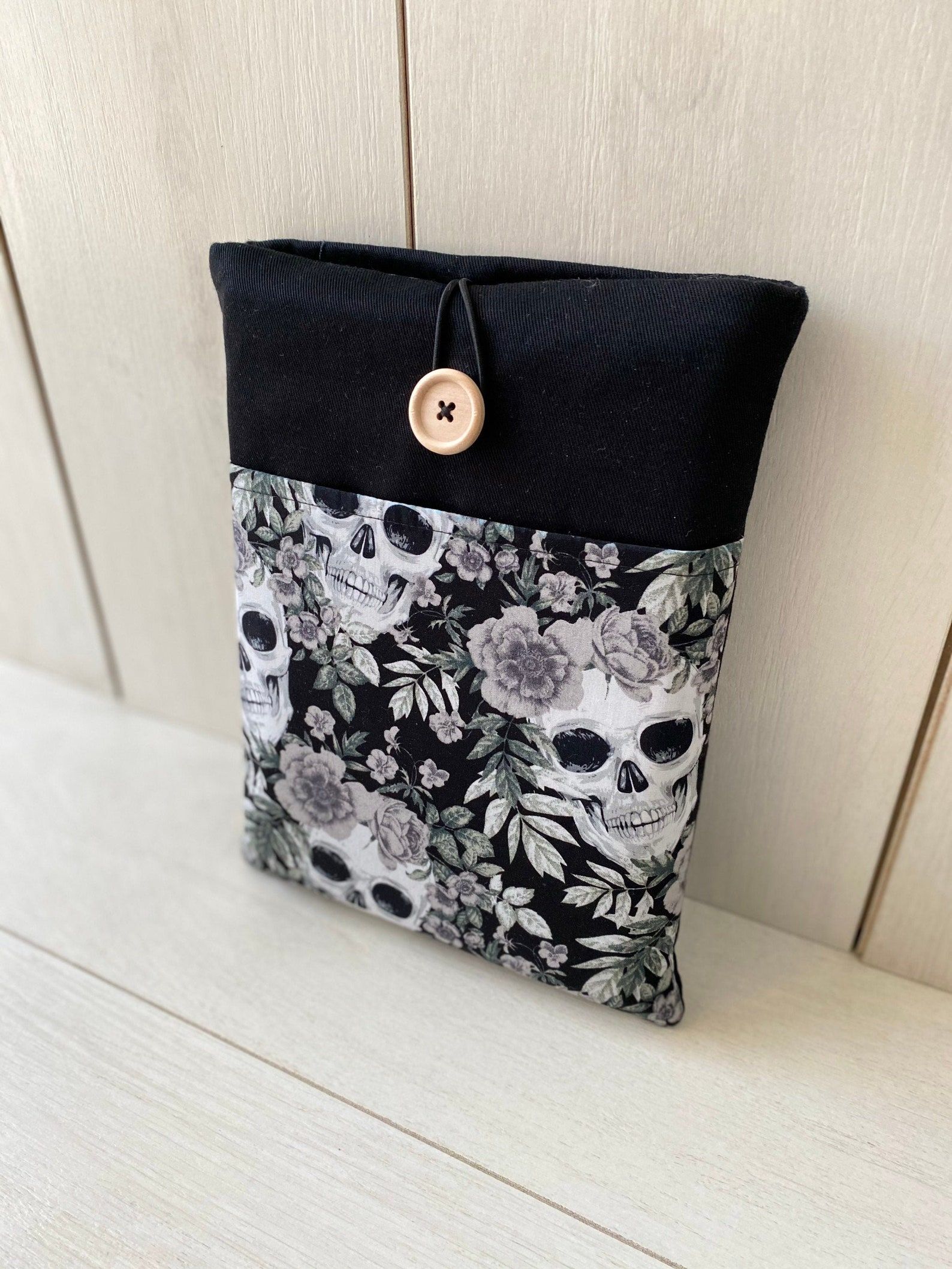 A book sleeve made in black and grey skulls and roses, with black accents and a button closure.