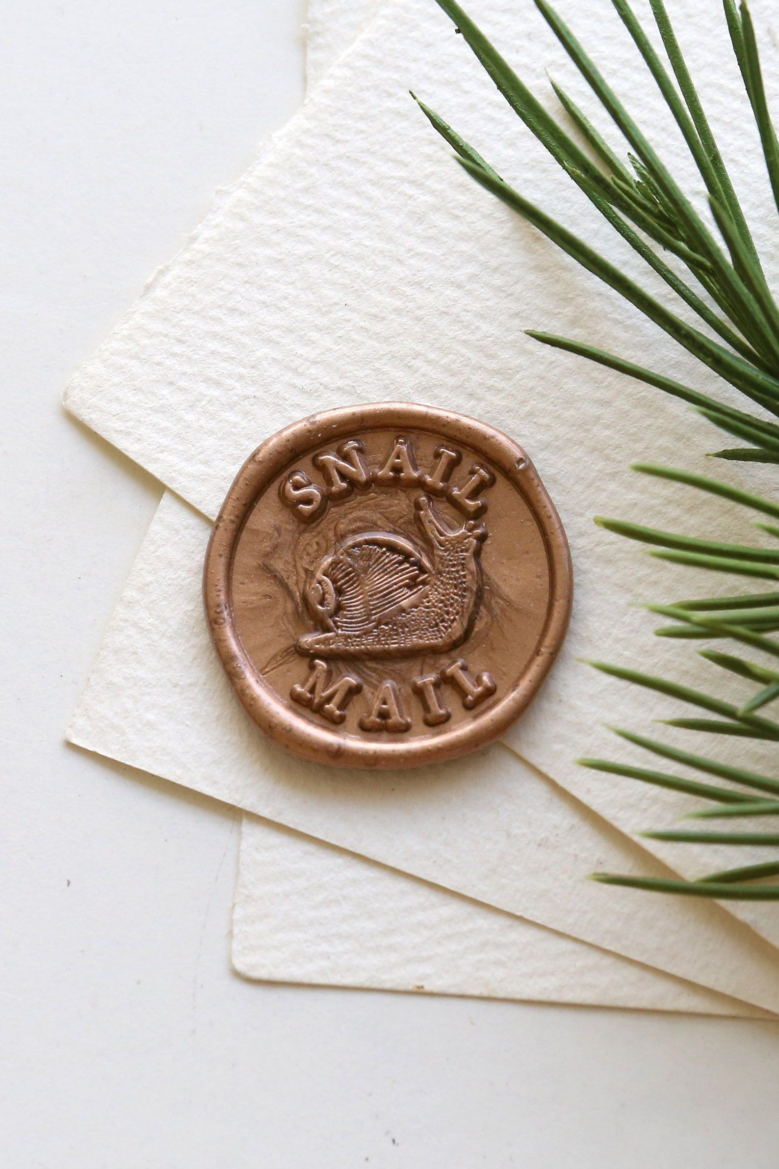 Image of a wax stamp. The center of the stamp has a snail, and the stamp reads "snail mail." 