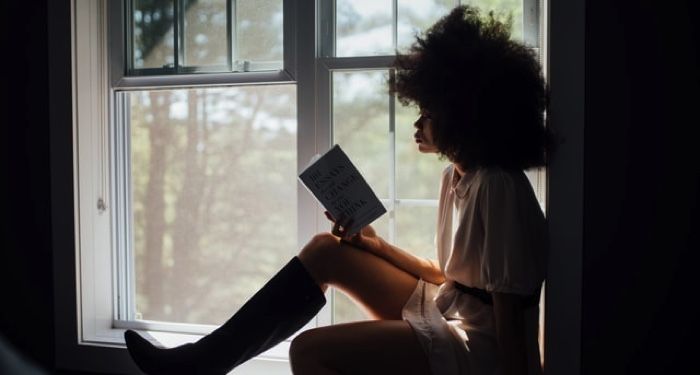 Black woman with glorious afro reading a book in a windowsill