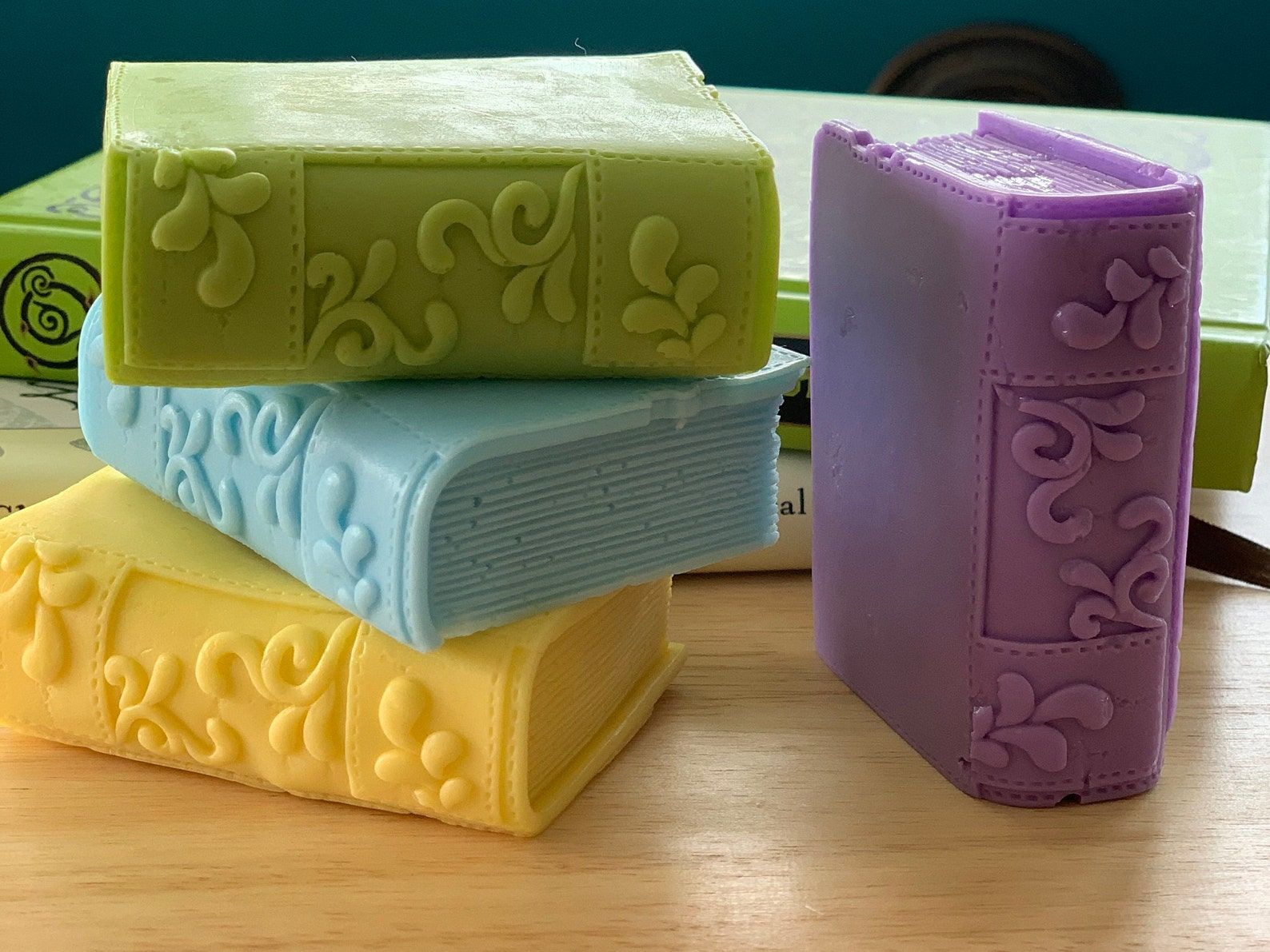 Four book-shape soap bars in yellow, blue, green, and purple. 