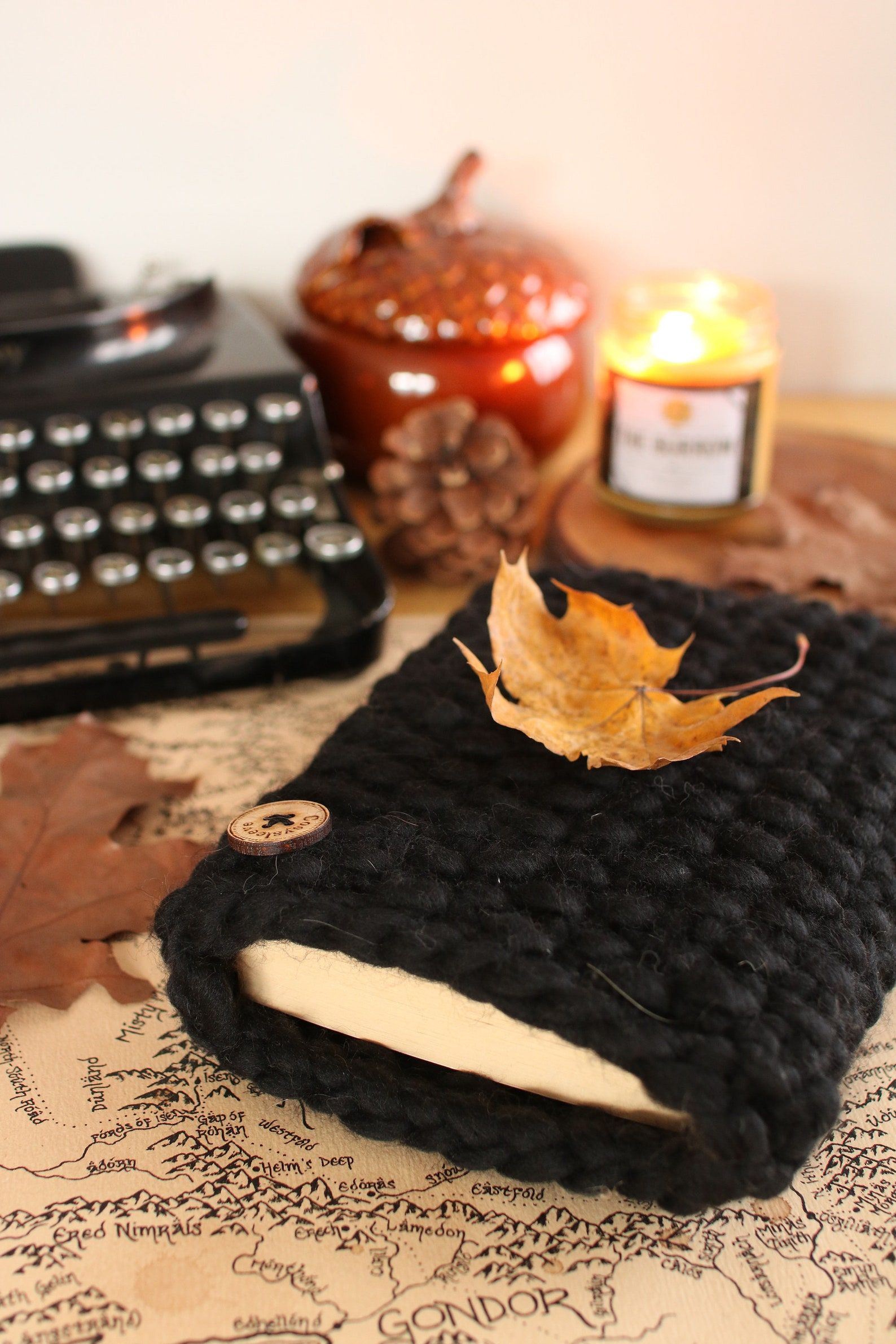 Image of a knitted black book sleeve with a single wooden button. It is lying on top of a map. 