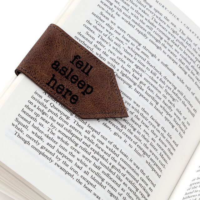 Image of a brown leather bookmark magnet. It reads "fell asleep here" in black ink. 