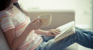 image of a young person with brown hair holding a tea cup and an open book on their lap