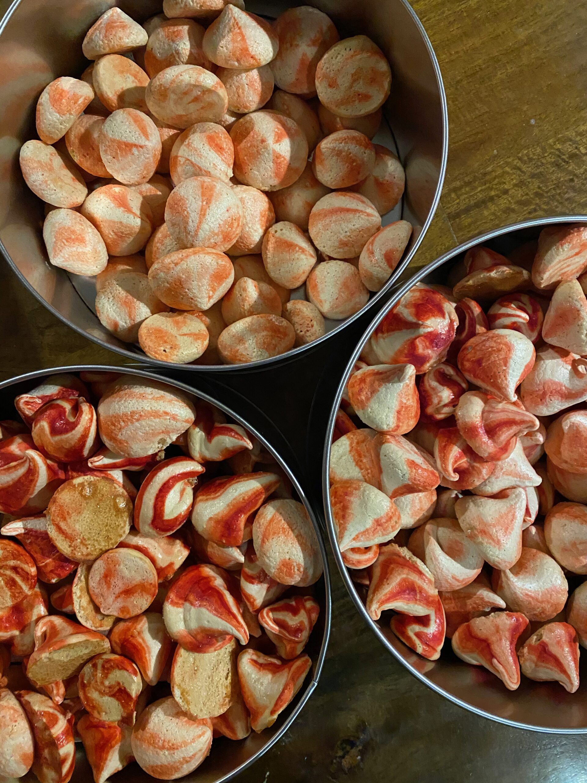 Three metal tins of small peppermint meringue kisses, swirled red and white.