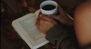 a person's hands holding a cup of coffee over an open book
