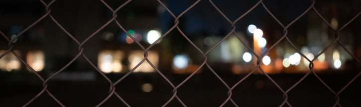 skyline at night seen through chainlink fence; image by ricky han for unsplash