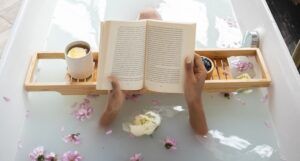 Black woman reading in bathtub with flower petals in the water and a mug on a tray
