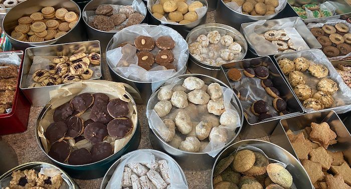 An array of cookies in metal tins on a counter. They cookies are all different shapes and sizes, including jam filled circles, star-shaped cookies, pinwheel cookies, and chocolate cookies.