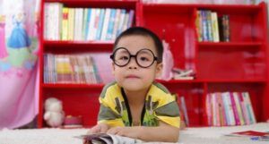 little Asian kid with round black glasses reading