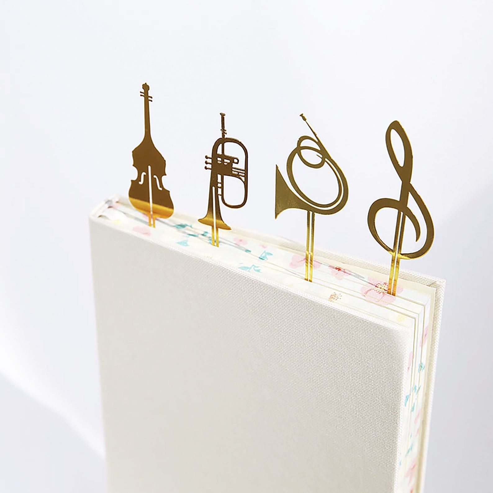 Image of four metal bookmarks, including a violin, trumpet, french horn, and treble clef, on top of a book. 