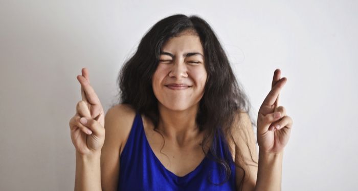 woman in a blue tank top with her eyes closed and fingers of both hands crossed
