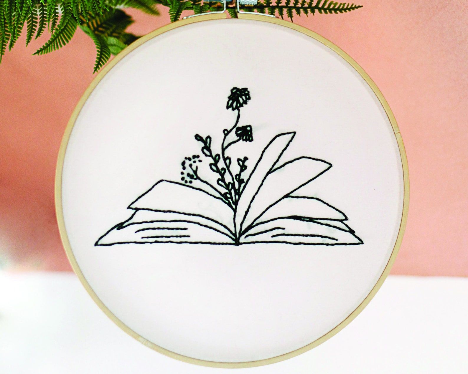 Image of an embroidery hoop. The design is of an open book with flowers growing out of it. 