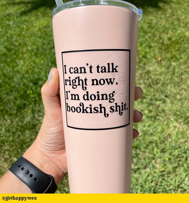 Image of a white hand holding a water bottle. The sticker on it reads in black font "I can't talk right now. I'm doing bookish shit."