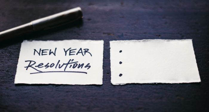 a pen and two small rectangles of paper. The sheet on the left says "New Year Resolutions" and the one on the right contains three blank bullet points