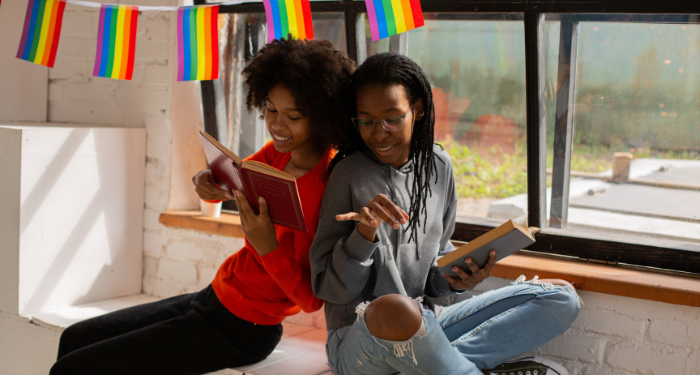 two Black femmes leaning on each other under small rainbow flags