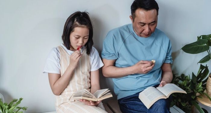 lightly tanned-skinned Asian father and daughter reading next to each other