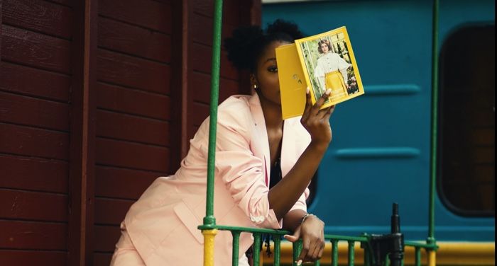brown-skinned woman with two afro puffs and a book on a brightly colored train,
