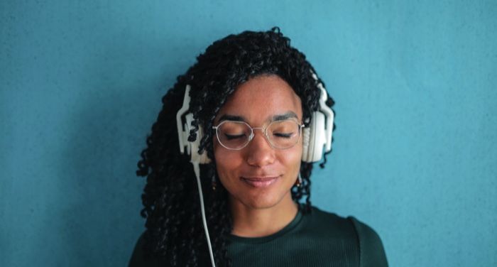 brown-skinned woman with headphones and big, kinky curly hair in front of a light blue wall