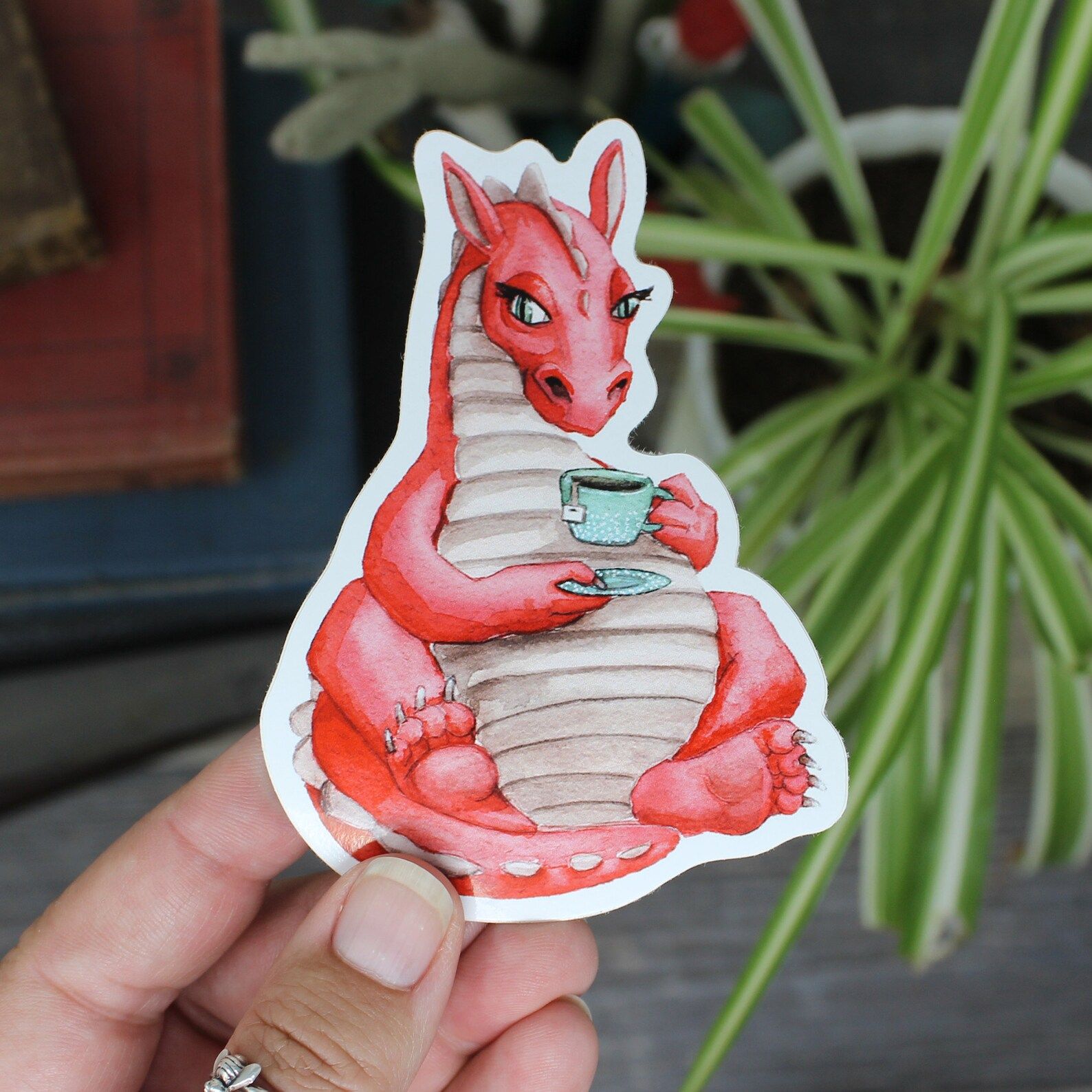 Etsy: A sticker featuring a cartoon-style dragon holding a cup of tea.