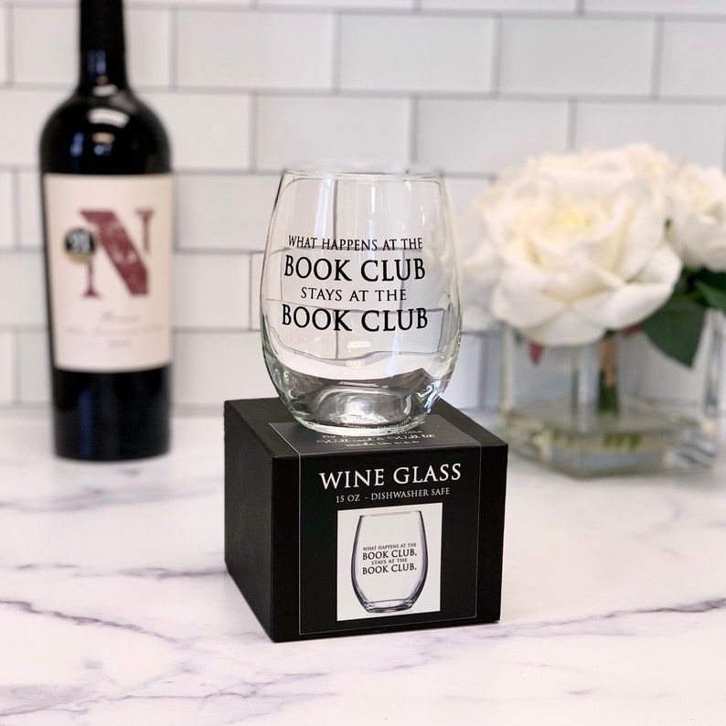 Image of a stemless wine glass that reads "what happens at book club stays at book club." It's on a white marble countertop. 