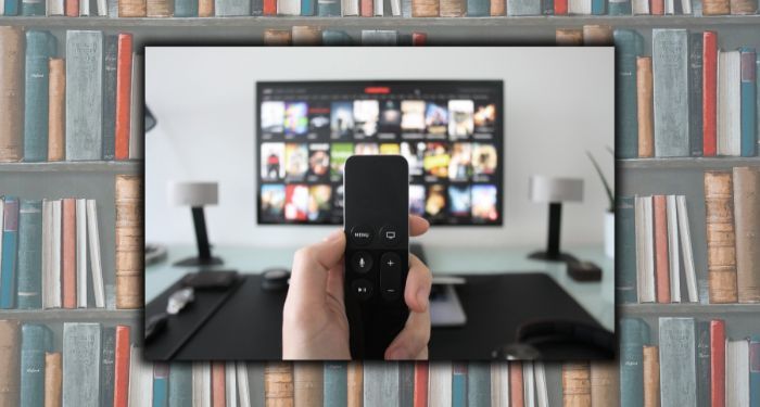 A hand holding a remote in front of a TV