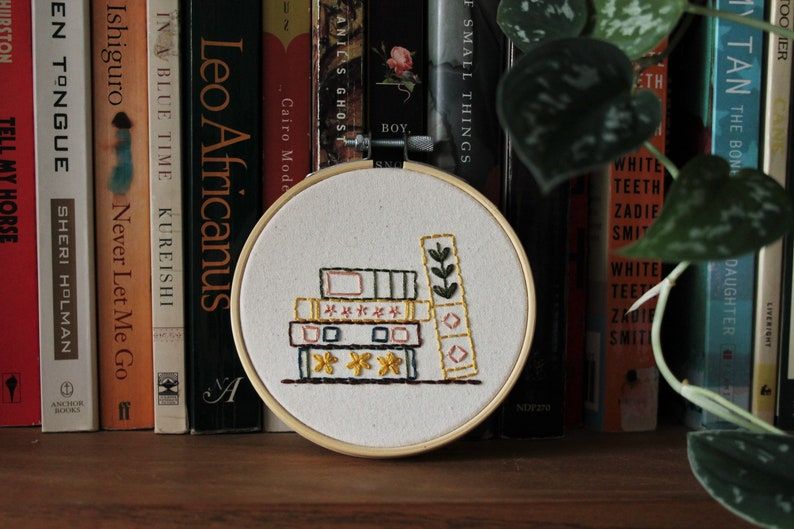Image of a stack of embroidered books. The finished pattern is against a shelf of books. 