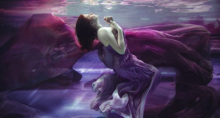 pale-skinned person underwater with a long, flow purple dress on