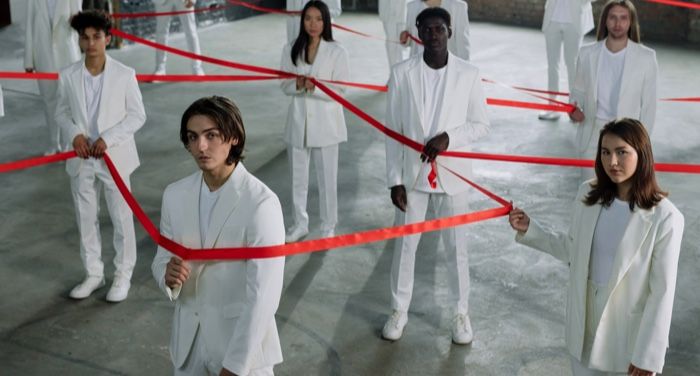a diverse group of people all dressed in white pantsuits holding parts of one long red ribbon