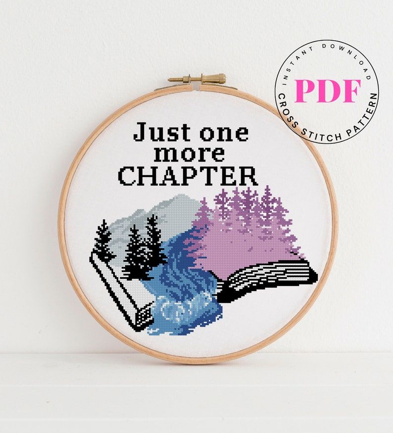 Cross stitch featuring an open book that has mountains and a river on it. The words "just one more chapter" are above the open book. 